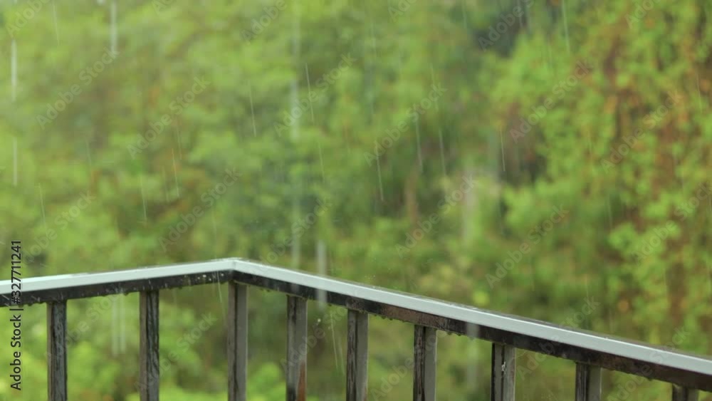A beautiful view from the balcony with rain falling on the railing and blurred dense greenery in the background. Static. A beautiful view from the balcony with rain falling on the railing and blurred dense greenery in the background. Static.