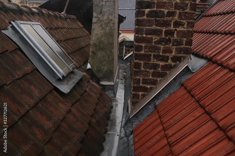 View from on the roofs of an old historical city that shows the beginning of two chmneys and a roof with new bright red tiles and a roof with already worn out dark red tiles View from on the roofs of an old historical city that shows the beginning of two chmneys and a roof with new bright red tiles and a roof with already worn out dark red tiles