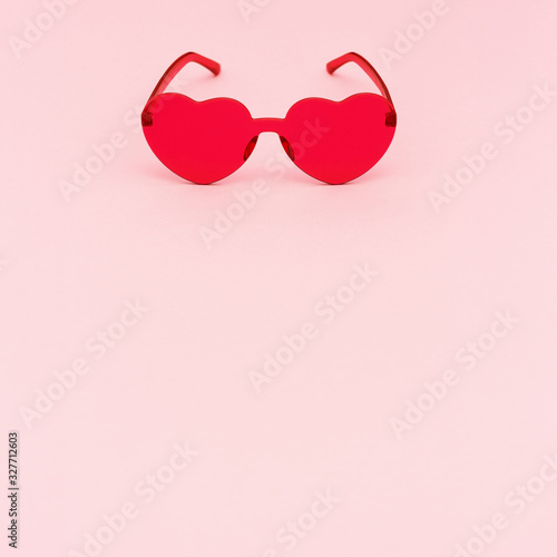 Stylish heart shaped glasses on pink background with copy space. Beautiful trendy red sunglasses. Fashion summer concept.