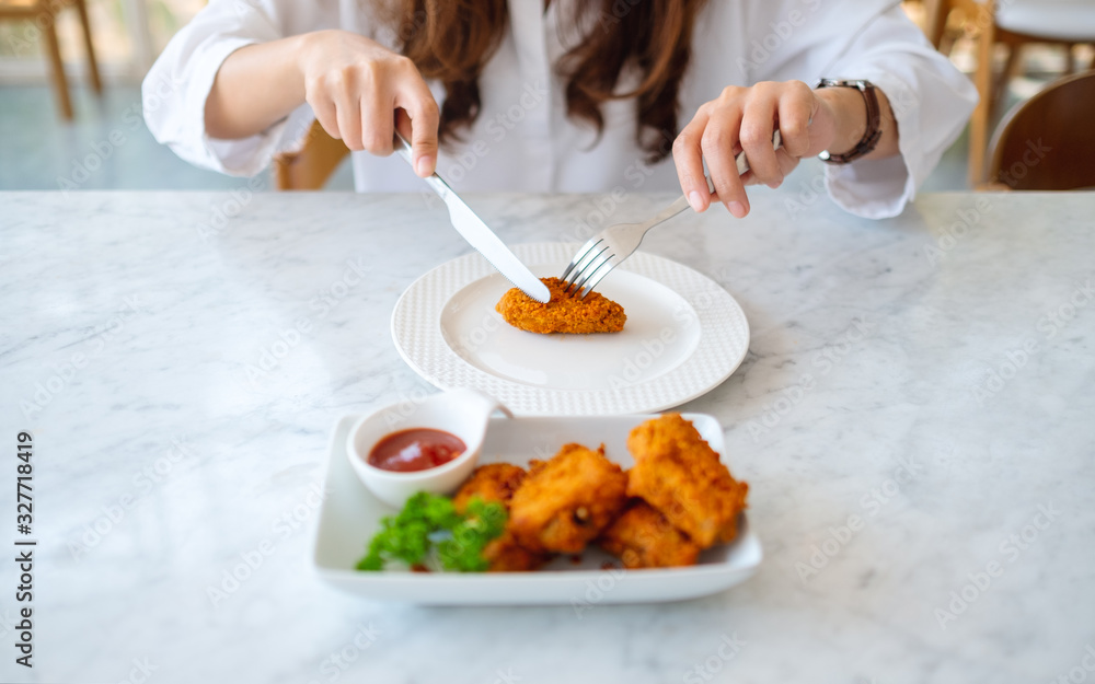 Closeup image of a woman using knife and fork to eat fried chicken in restauran