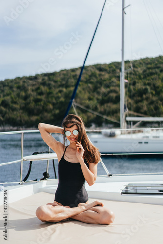Young healthy and calm woman doing yoga on sailing yacht boat in sea at island background