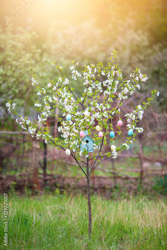 Beautiful decorative birdhouse in the branches of a blossoming cherry tree. Decorative easter eggs hanging on threads