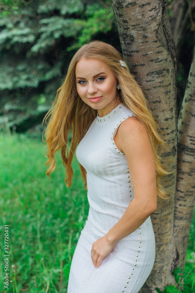 Portrait of a charming blond woman wearing beautiful white dress standing next to rowan tree. Portrait of a charming blond woman wearing beautiful white dress standing next to rowan tree.