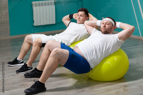 Tired fat man is lying on a fitness ball training during group fitness classes. Overweight