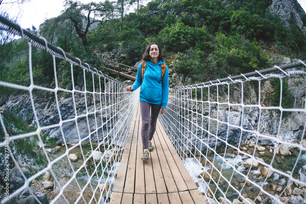 Naklejka premium A girl with a backpack crosses the canyon on a suspension bridge.