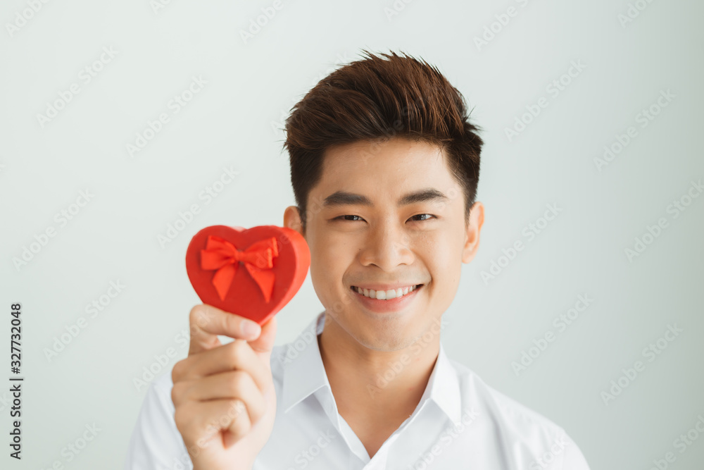 Handsome young man holding red heart box on white background