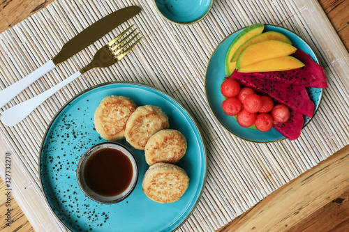 Vegan tofu cheese pancakes on blue plate with fresh tropical fruits and coconut cream, top view