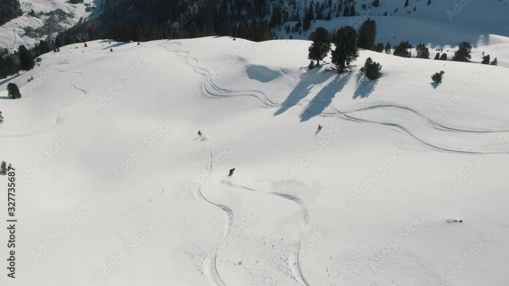 AERIAL: Snowboarders carve their way down the mountain slopes. Sunny winter day. Zillertal, Austria AERIAL: Snowboarders carve their way down the mountain slopes. Sunny winter day. Zillertal, Austria