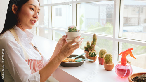 Young gardener woman holding a flowerpot of cactus in the room.