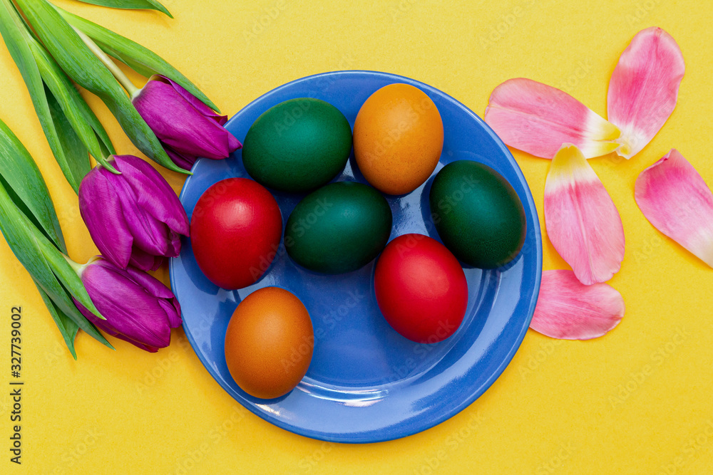 Easter eggs with tulips on a blue dish on a yellow background. Easter eggs with tulips on a blue dish on a yellow background.