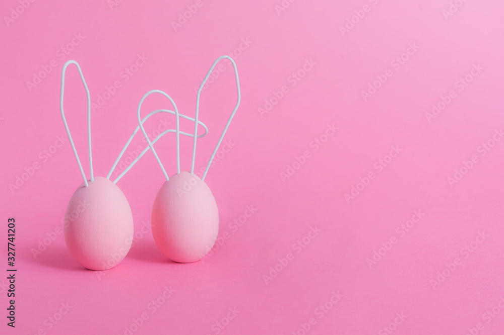 Two Easter pink eggs with rabbit ears made of wire and on a pink monochrome isolated background. Happy Easter concept, minimalism. Gentle postcard in calm colors, a place to copy.