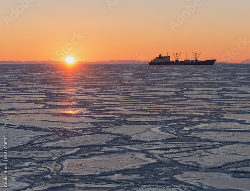 Dawn in the Sea of Okhotsk, ship on the horizon, in the sea ice