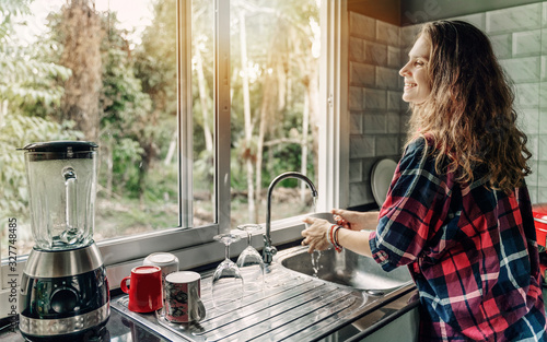 Obraz na plátně A woman washes dishes in her house, a sink in front of a window overlooking a su