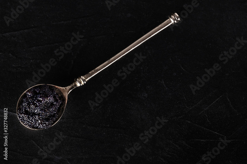 Black caviar in a silver spoon, shot from above on a dark background with a place for text