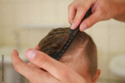 The hairdresser combs the boy with a black comb. Boy haircut