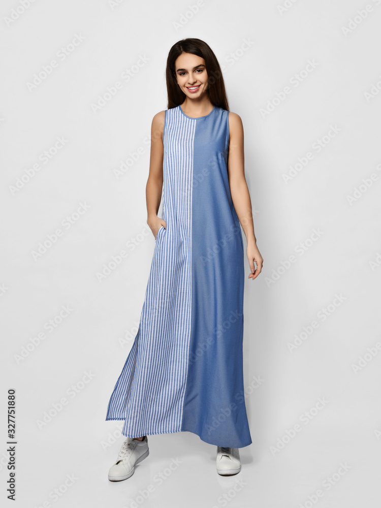 Happy young woman is posing in new fashion long maxi  summer blue-and-white-striped dress over gray