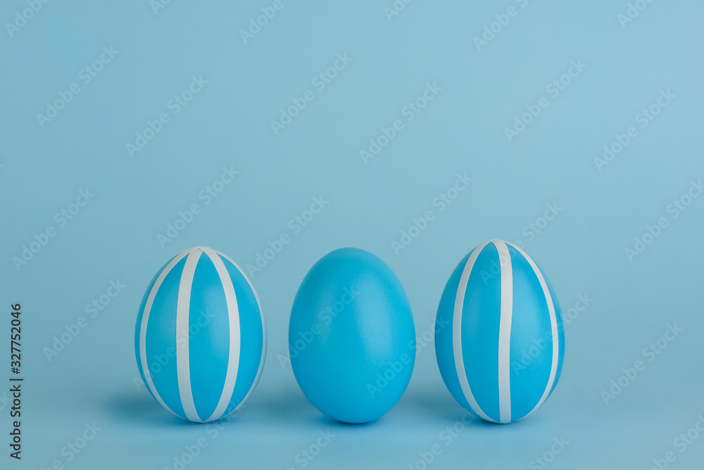 Three Easter decorated blue eggs. Striped blue eggs in a row on a blue background. White strips. Copy space. Blue monochrome . Three Easter decorated blue eggs. Striped blue eggs in a row on a blue background. White strips. Copy space. Blue monochrome .