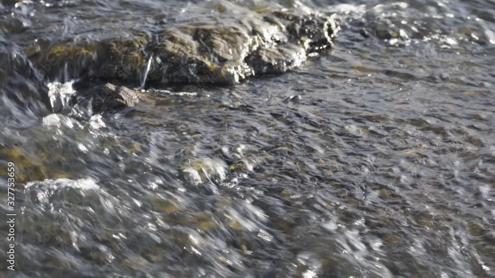 The rapid flow of the river over the stones. Close-up. Small waterfall over a fast stream of water. The rapid flow of the river over the stones. Close-up. Small waterfall over a fast stream of water.