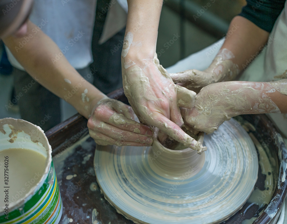 Hands working with clay on a Potter's wheel, close-up. Teamwork in the workshop