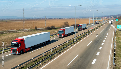 Convoy of transportation trucks passing on a highway on a bright blue day. Highway transportation with white lorry tracks