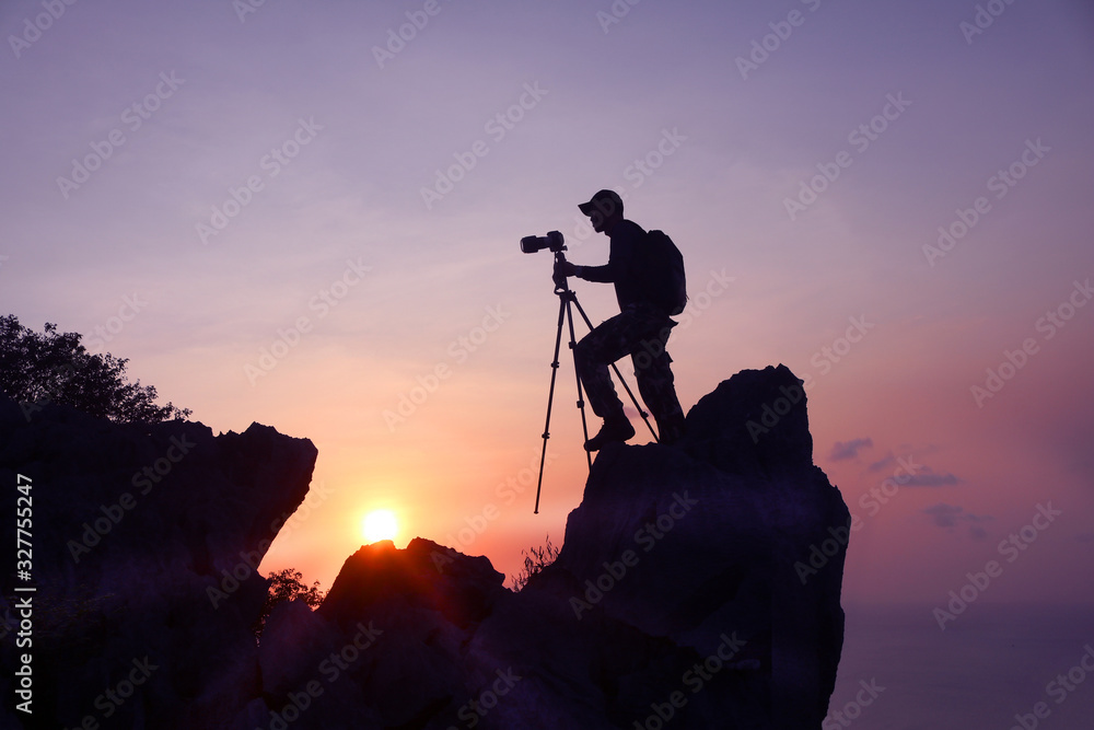 Photographer climbing on the top of the mountain to take a picture at sunset. - obrazy, fototapety, plakaty 
