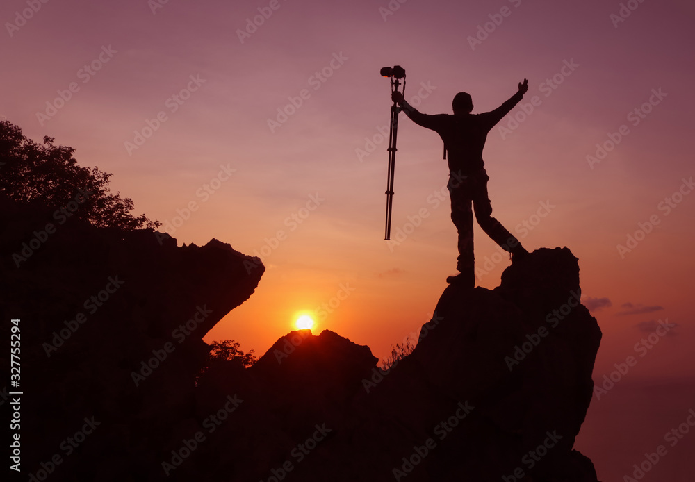 Photographer climbing on the top of the mountain to take a picture at sunset.