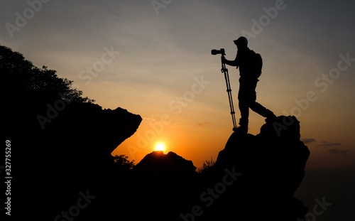 Photographer climbing on the top of the mountain to take a picture at sunset.