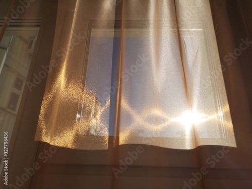 Bright sun with highlights shining through the Golden tulle on the background of the window