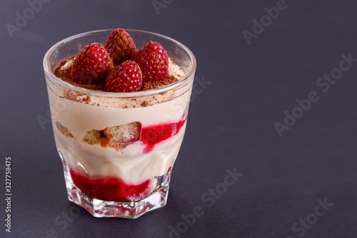 Billede på lærred Italian dessert panna cotta with raspberries and cocoa powder served in small glass over black background