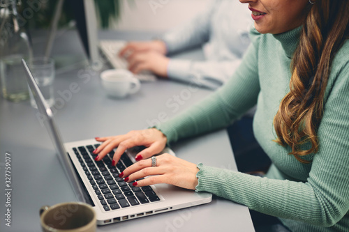Two coworkers smiling and typing on computer in office.	