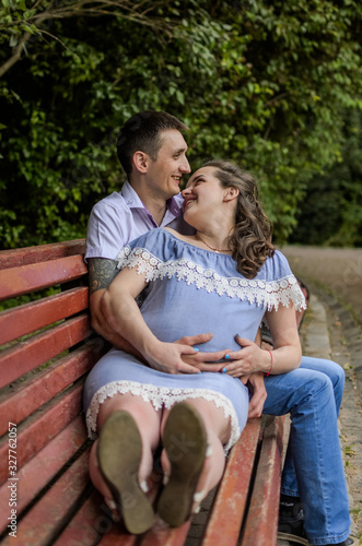 Young couple in love, husband and pregnant wife on a bench in the park, happy family
