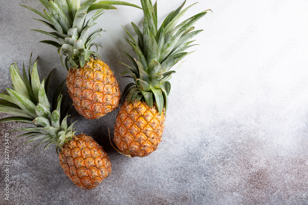 Three whole fresh ripe pineapples on concrete background. Food background. Top view, copy space. Three whole fresh ripe pineapples on concrete background. Food background. Top view, copy space.