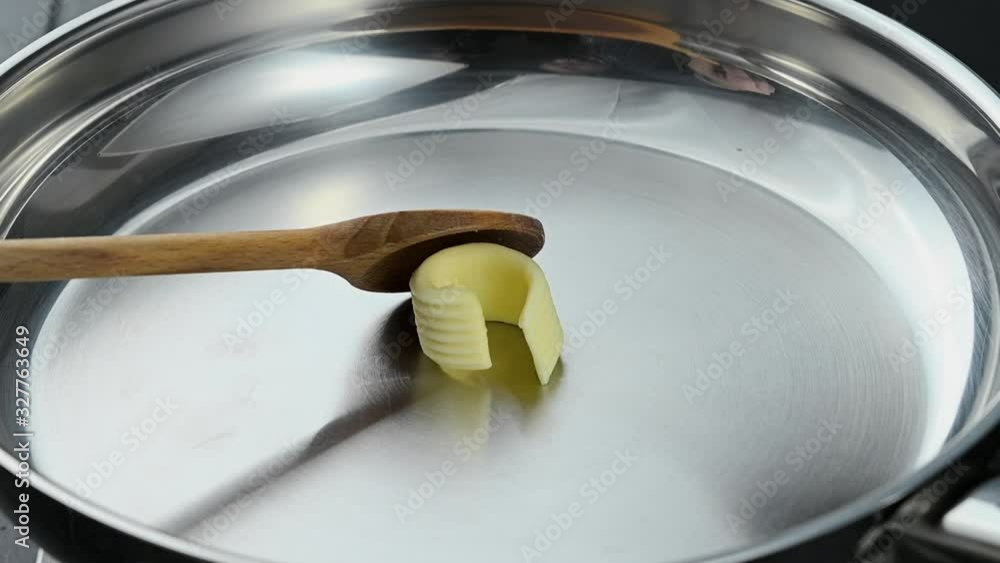 Neues PrSlow motion placing a curl of butter in a hot frying pan with a wooden spoon where it starts to melt over the heat in a food preparation conceptojekt Neues PrSlow motion placing a curl of butter in a hot frying pan with a wooden spoon where it starts to melt over the heat in a food preparation conceptojekt