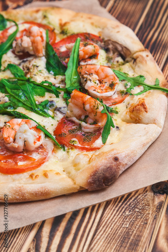 Italian pizza with royal prawns, tomatoes, cheese, pesto and arugula on a classic dough on a wooden table close-up