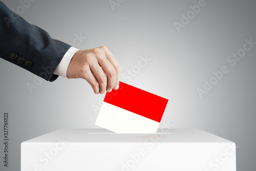 Man putting a voting ballot into a box with Indonesian flag.