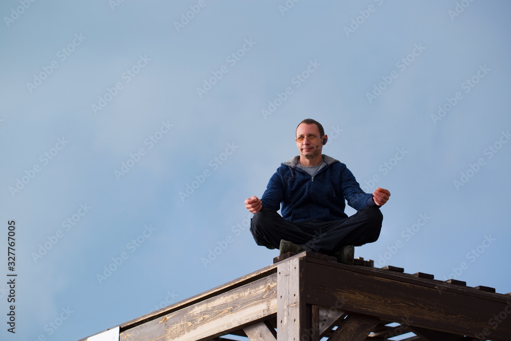Fototapeta premium Young athletic man meditating, against blue sky background