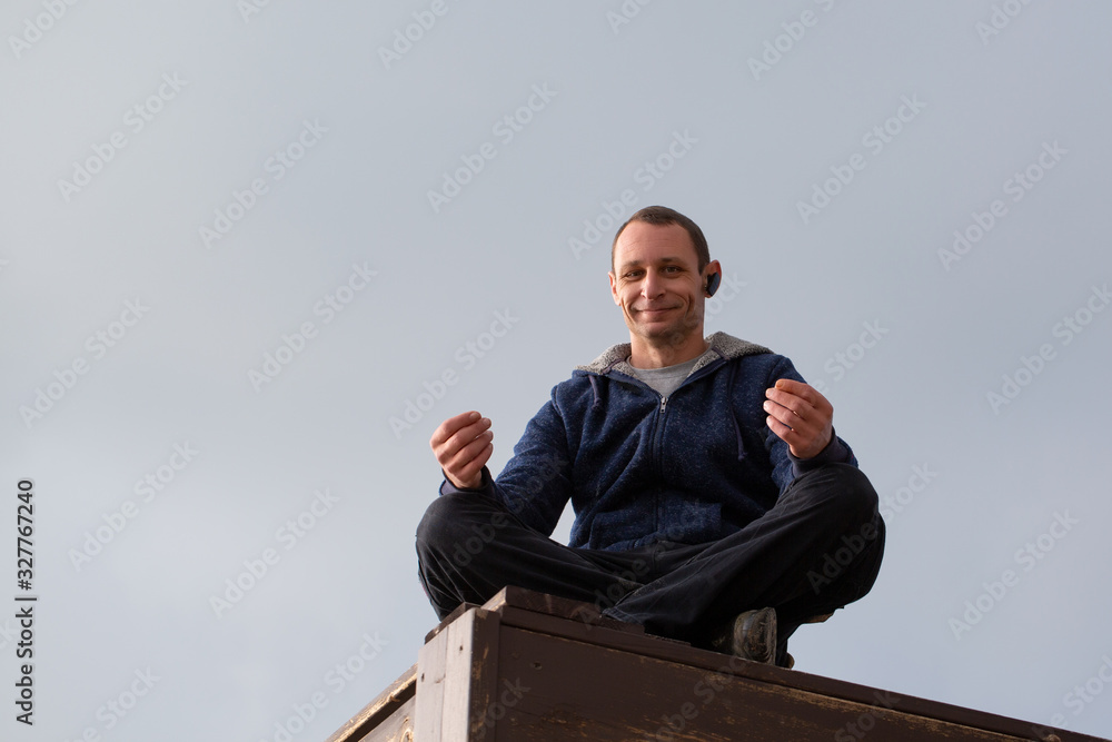 Young athletic man meditating, against blue sky background