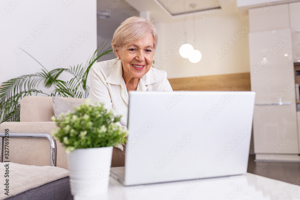 Elderly lady working with laptop. Portrait of beautiful older woman working laptop computer indoors. Senior woman using laptop at home, laughing Elderly lady working with laptop. Portrait of beautiful older woman working laptop computer indoors. Senior woman using laptop at home, laughing