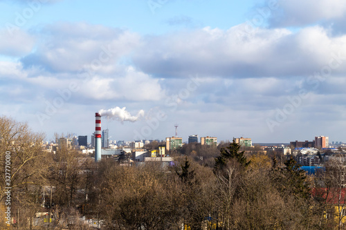Urban landscape with a beautiful sky in the clouds and a boiler room chimney with smoke in early spring in Europe. View of the city from a tall building.