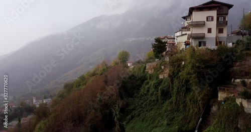 Residential Houses At The Edge Of The Lush Mountain In The Town Of Crandola, Valsassina Italy On A Foggy Day - Aerial Shot photo