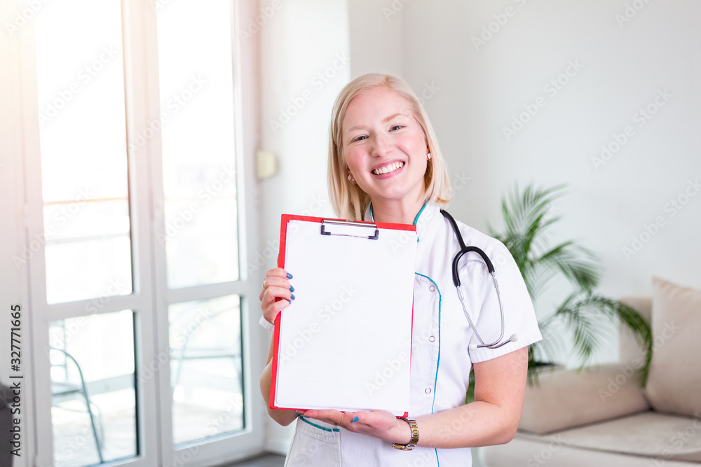Female doctor holding clip board and smiling. Woman doctor standing straight in home care hospital. Close-up of a female doctor using clip board with stethoscope around her neck Female doctor holding clip board and smiling. Woman doctor standing straight in home care hospital. Close-up of a female doctor using clip board with stethoscope around her neck