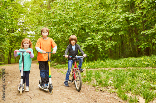 Drei Kinder mit Roller und Fahrrad im Park