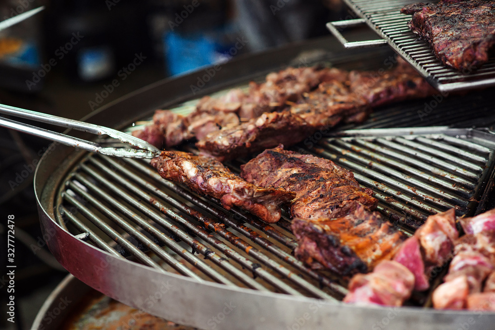 Chef preparing meat on the grill. Food catering, party. Street festival. Barbeque, BBQ concept. Male hand with tongs holding hot pork ribs. Street food. Chef preparing meat on the grill. Food catering, party. Street festival. Barbeque, BBQ concept. Male hand with tongs holding hot pork ribs. Street food.