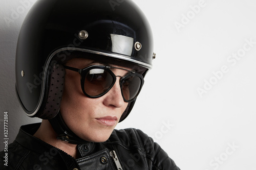 Close-up portrait of attractive biker woman posing on the white wall. Indoor. © face_reader_img