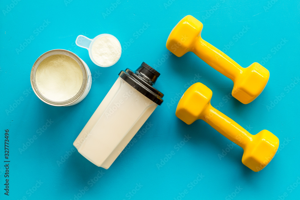 Sport nutrition. Whey protein, shaker, dumbbells on blue background top-down flay lay Sport nutrition. Whey protein, shaker, dumbbells on blue background top-down flay lay