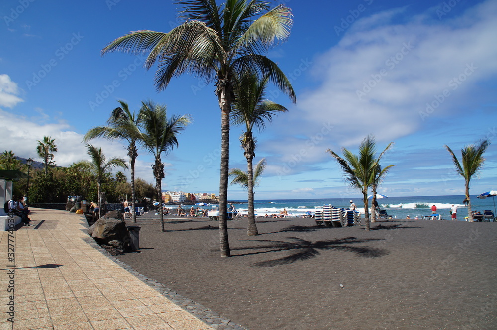 picturesque Playa Jardín beach on the Spanish Canary Island Tenerife with black volcanic sand blue ocean water and green palm trees