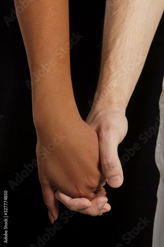 Racism is a poison which envenoms our society with prejudice and hate. A close-up symbolic photo of dark and white-skinned hands. The female and male wrists joined on the black background. © RedUmbrella&Donkey