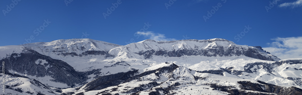 Panorama of high snowy mountains and blue sky with clouds at sun winter day