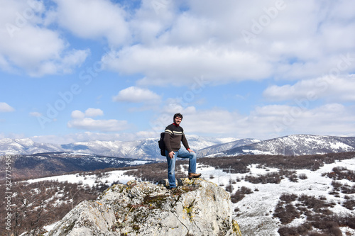 Young man enjoy in outstanding view on mountains in spring. Climber on top of mountain. Man standing on edge of rock and look into mountain