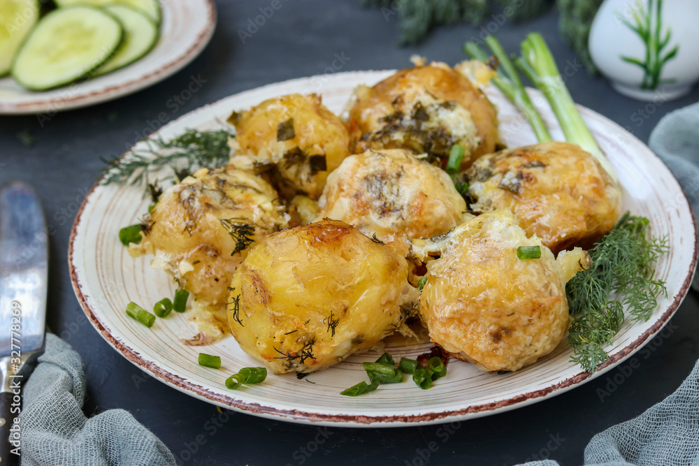 Baked young potatoes with cheese and dill in a plate against a dark background Baked young potatoes with cheese and dill in a plate against a dark background
